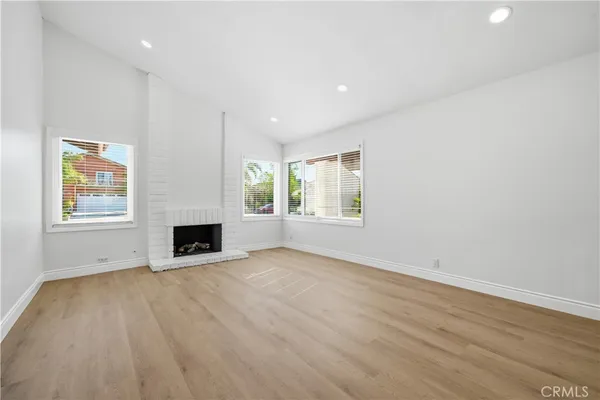 an empty room with wooden floor fireplace and windows