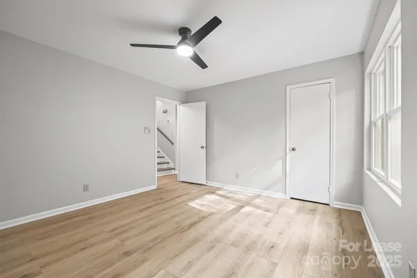 an empty room with wooden floor ceiling fan and windows
