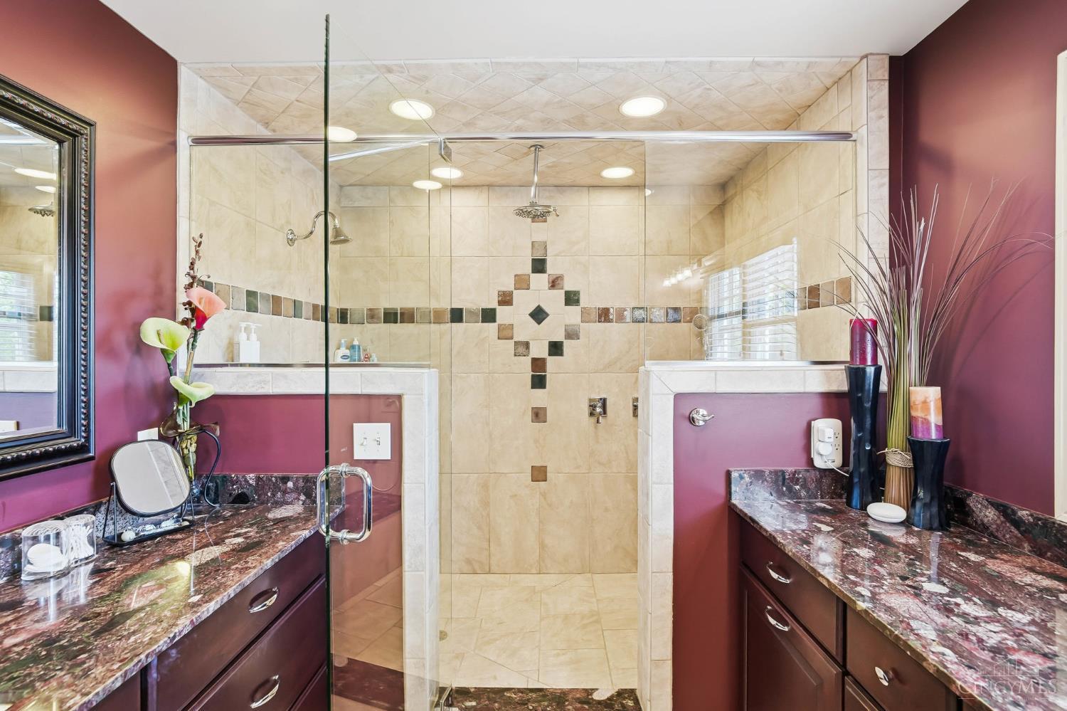 2780 Walsh Road Cincinnati, OH 45208 - Photo 31 of 68 The ensuite bath is thoughtfully designed with both comfort and functionality in mind, featuring dual vanities with rich cabinetry and expansive granite countertops that provide ample space for everyday routines. Warm, sophisticated finishes are complemented by abundant natural light, creating a bright yet inviting atmosphere. The oversized walk-in shower serves as a true focal point, showcasing full tile surround, decorative inlay accents, multiple shower heads, and a built-in bench for added convenience. A private water closet enhances the layout, offering both privacy and practicality, while generous storage throughout completes this well-appointed primary bath.