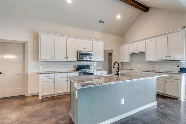 a kitchen with kitchen island granite countertop a sink white cabinets and stainless steel appliances