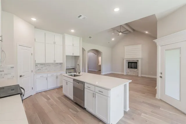 a large white kitchen with a stove a sink dishwasher and a refrigerator with wooden floor