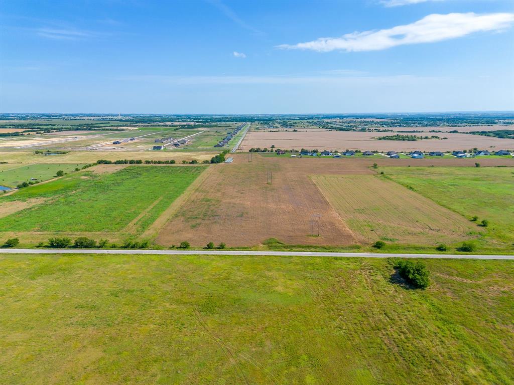 6785 Hoehn Road Valley View, TX 76272 - Photo 4 of 14 Expansive undeveloped land featuring a paved road frontage, diverse vegetation including cultivated fields and grassy areas, and distant residential structures under a clear sky