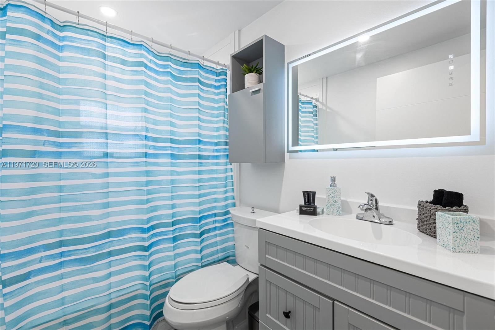 2770 Northeast 30th Street Lighthouse Point, FL 33064 - Photo 20 of 27 a bathroom with a sink a toilet a mirror and shower curtain