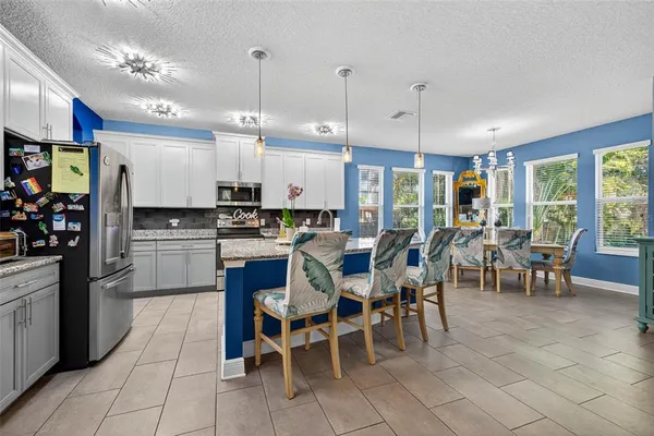 a kitchen with stainless steel appliances kitchen island granite countertop a table chairs and a refrigerator