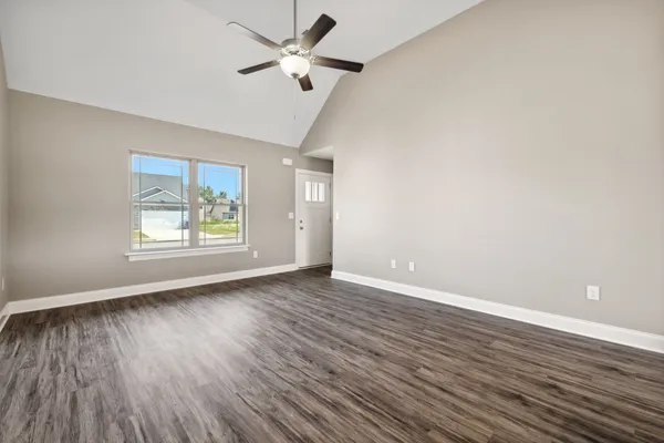 an empty room with wooden floor fan and windows