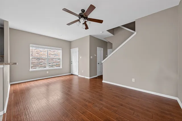 an empty room with wooden floor fan and windows
