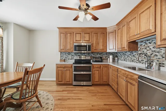 a kitchen with stainless steel appliances granite countertop a stove top oven a sink dishwasher a dining table and chairs with wooden cabinets