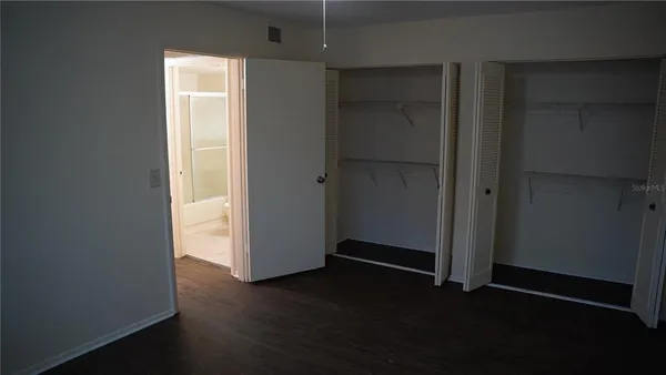 an empty room with wooden floor closet and windows