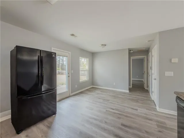 a view of an empty room with wooden floor and a kitchen