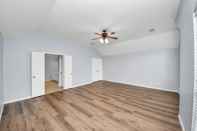 an empty room with wooden floor chandelier fan and windows