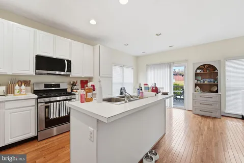 a kitchen with stainless steel appliances a stove top oven a sink a refrigerator white cabinets and wooden floor