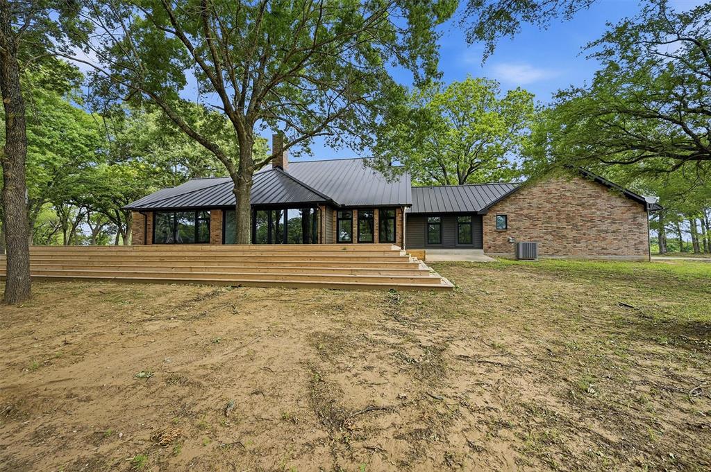410 Arkansas Road Sadler, TX 76264 - Photo 32 of 40 Contemporary residence featuring a black metal roof, brick and dark siding exterior, and extensive back decking