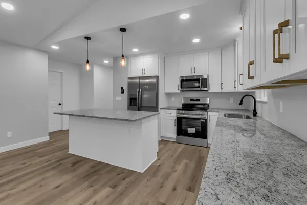 a kitchen with granite countertop a stove top oven a sink a refrigerator and white cabinets with wooden floor