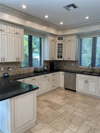 a large kitchen with granite countertop a stove a sink a window and white cabinets