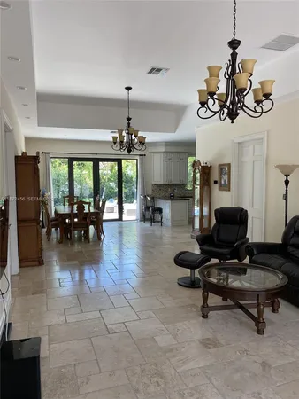 a living room with couches a dining table and a chandelier with kitchen view