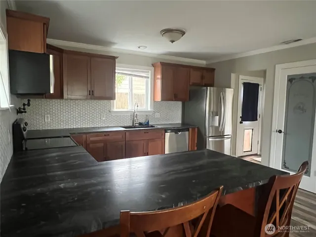 a kitchen with stainless steel appliances granite countertop a sink a stove a refrigerator with a dining table and chairs