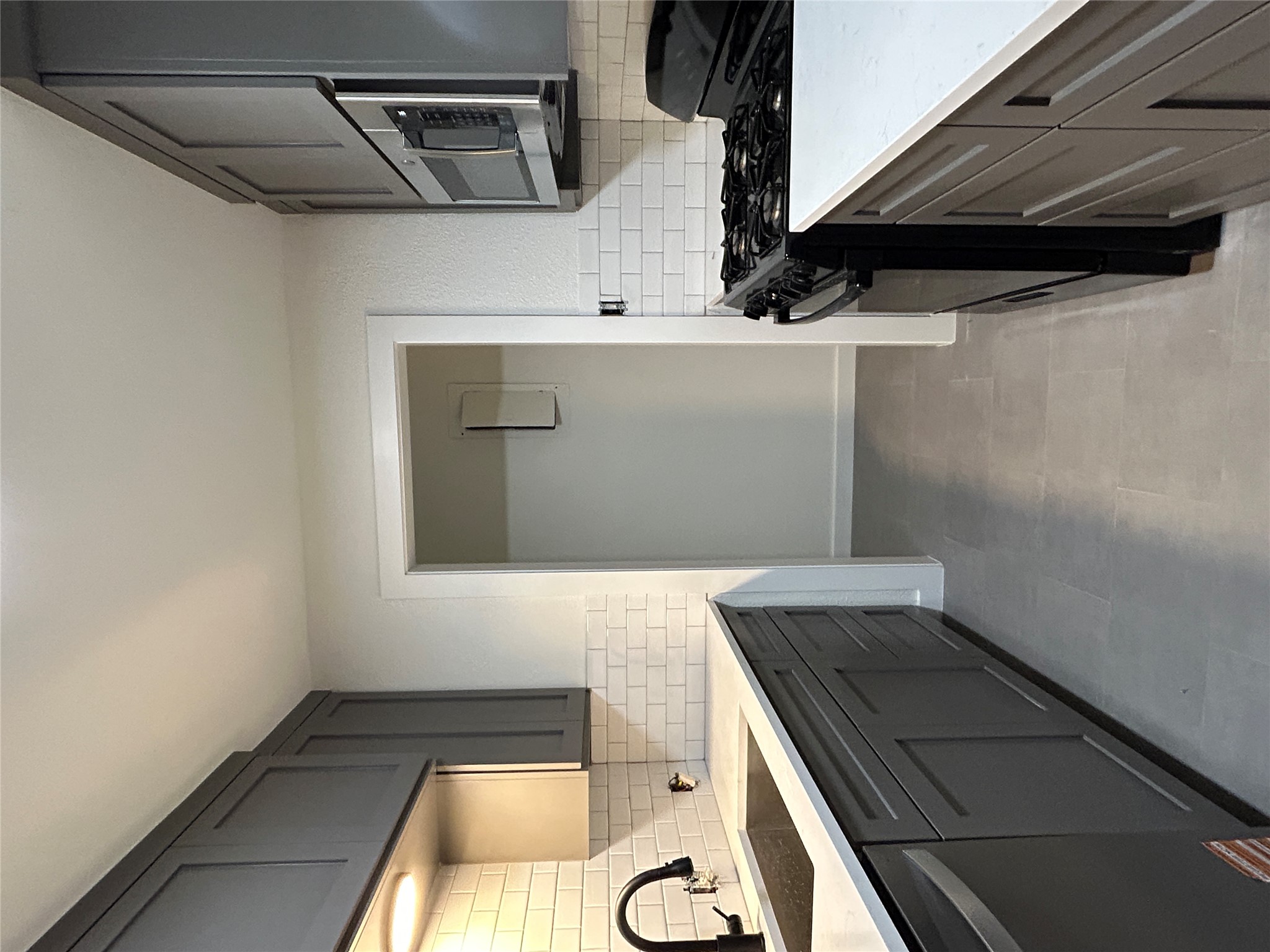 Galley kitchen featuring gray shaker cabinetry, white subway tile backsplash, and light-colored countertops