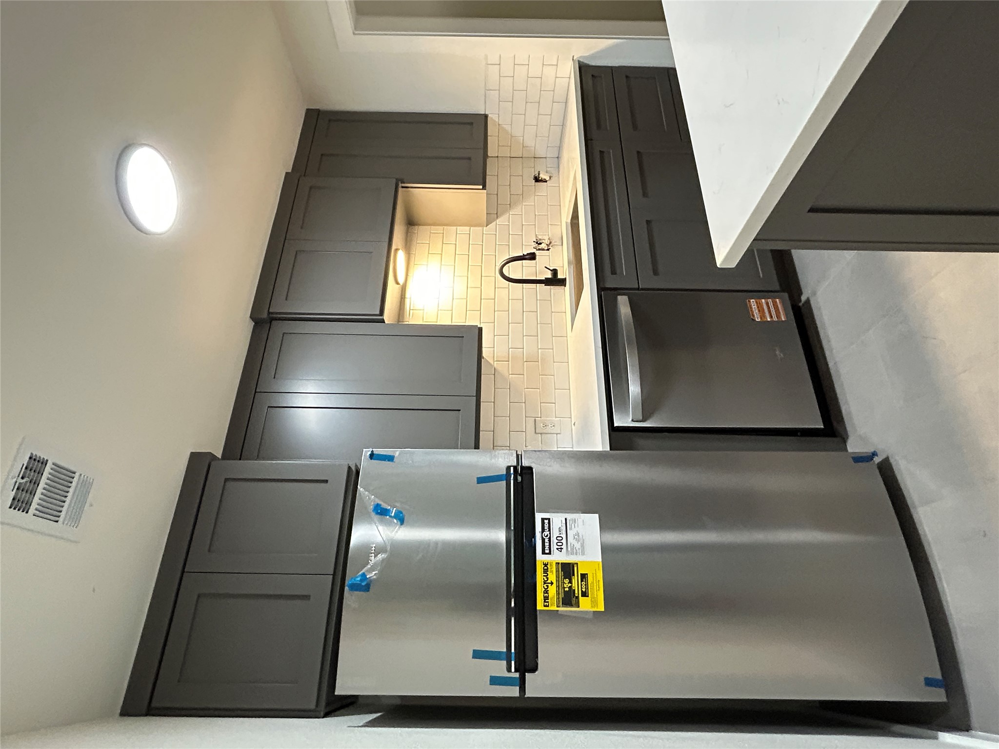 6502 South 1st Street, Unit 101 Austin, TX 78745 - Photo 3 of 12 Modern kitchen featuring dark grey cabinetry, white subway tile backsplash, stainless steel appliances, a stainless steel sink with a matte black faucet, and white countertops