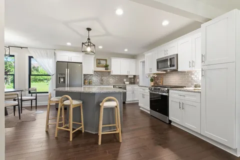 a kitchen with kitchen island granite countertop wooden floors white cabinets and stainless steel appliances