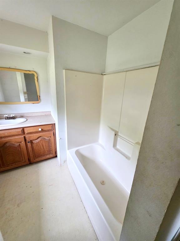 417 West Huffman Street Krum, TX 76249 - Photo 15 of 26 White acrylic bathtub with integrated shower surround, vanity with wood-finish cabinetry, and a countertop with an undermount sink