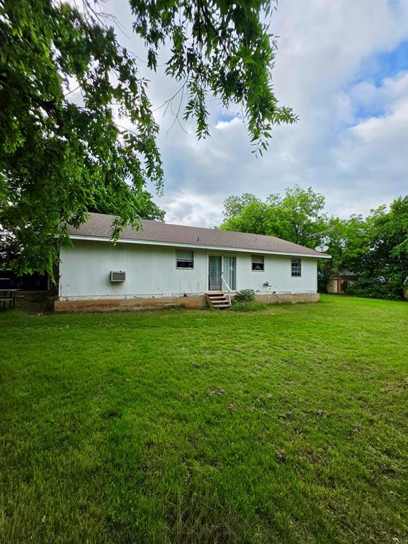 417 West Huffman Street Krum, TX 76249 - Photo 19 of 26 Expansive rear yard featuring a verdant lawn, mature trees, and a residential structure with white siding