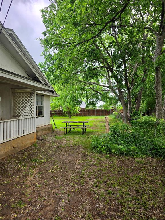 417 West Huffman Street Krum, TX 76249 - Photo 20 of 26 Spacious backyard featuring mature trees, a wood privacy fence, and an exterior wall with lattice detailing