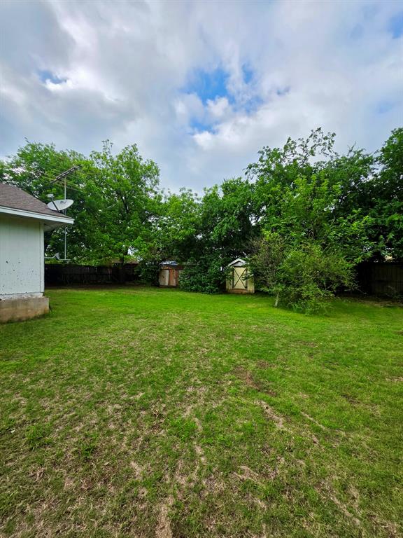 417 West Huffman Street Krum, TX 76249 - Photo 22 of 26 Spacious backyard featuring a grass lawn, mature trees, and two storage sheds