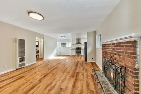 a view of empty room with wooden floor and kitchen