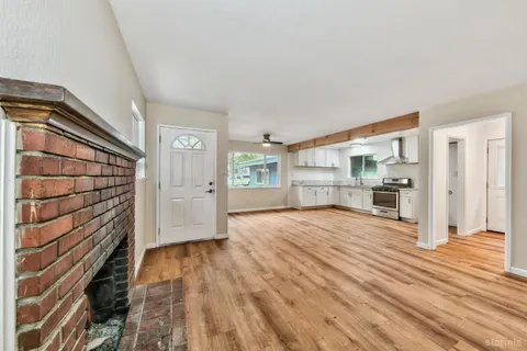 a view of empty room with wooden floor and kitchen