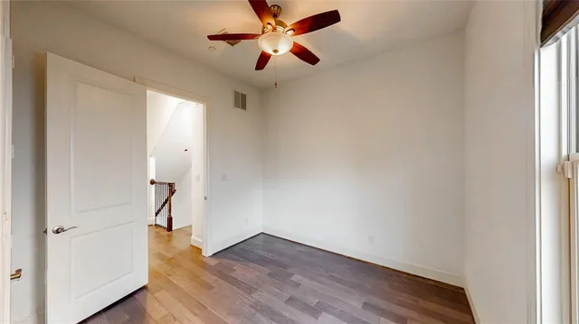 an empty room with wooden floor a ceiling fan and windows