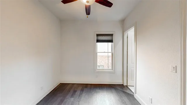 an empty room with wooden floor chandelier fan and windows