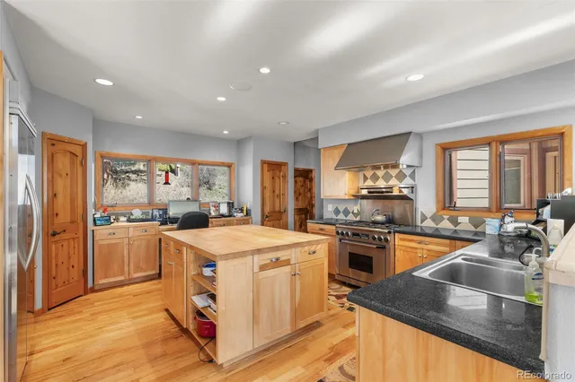 a kitchen with stainless steel appliances granite countertop a stove top oven a refrigerator a sink and dishwasher with wooden floor