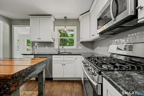 a kitchen with stainless steel appliances granite countertop a stove a sink dishwasher and cabinets with wooden floor