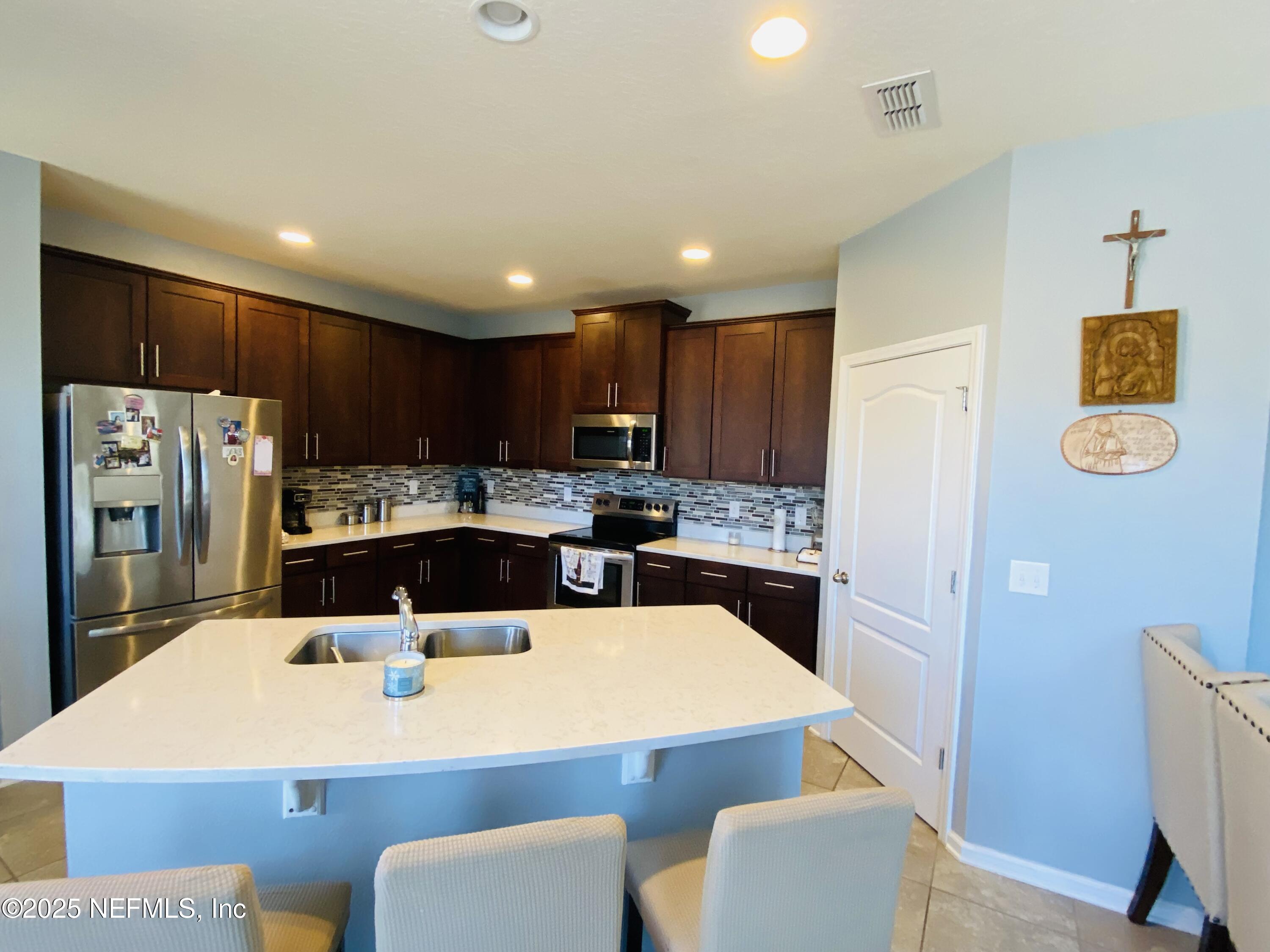 99 Bush Place St. Johns, FL 32259 - Photo 5 of 21 a kitchen with stainless steel appliances kitchen island granite countertop a refrigerator a stove a sink dishwasher with a dining table and chairs