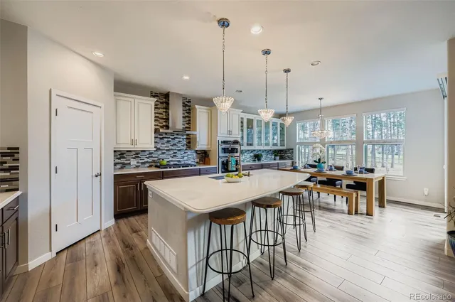 a open kitchen with stainless steel appliances granite countertop a stove a refrigerator a kitchen island a dining table and chairs with wooden floor