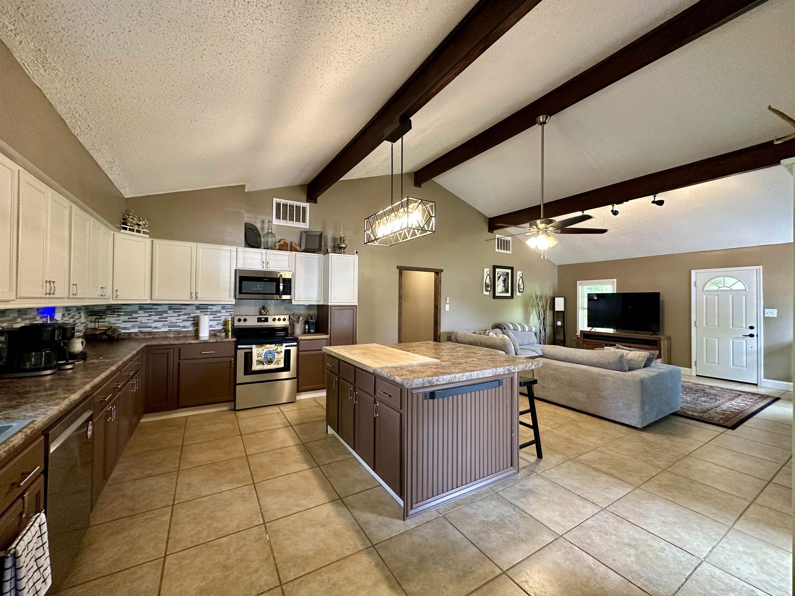 1230 Joann Road Somerville, TN 38068 - Photo 8 of 29 Open-concept kitchen and living area featuring vaulted ceilings with exposed beams, tile flooring, a kitchen island with seating, a stainless steel range and microwave, and a two-tone cabinetry scheme