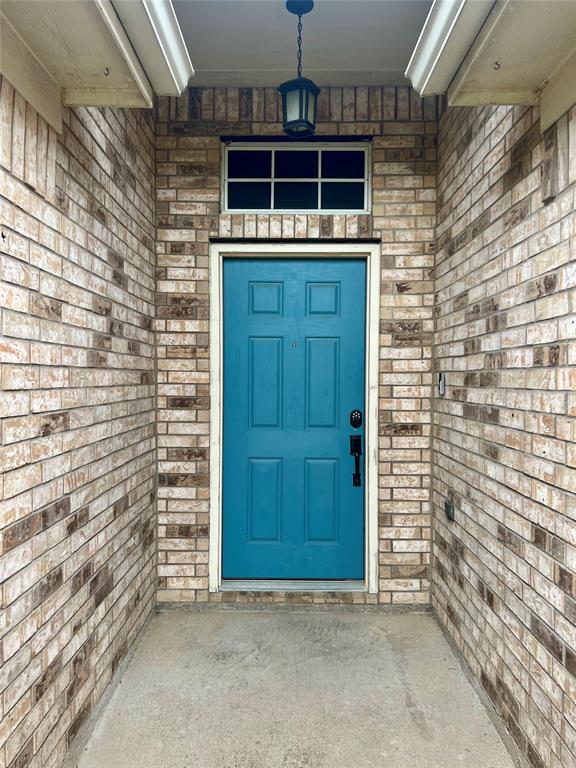 12201 Rolling Ridge Drive Fort Worth, TX 76028 - Photo 4 of 21 Inviting entryway featuring a vibrant teal paneled door, brick facade, transom window, and an overhead lantern light fixture