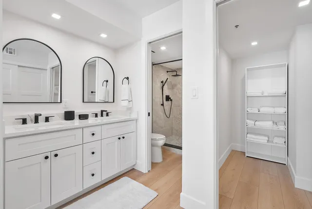 a spacious bathroom with 2 sink a toilet and a large mirror