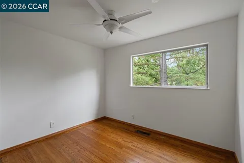 an empty room with wooden floor chandelier fan and windows