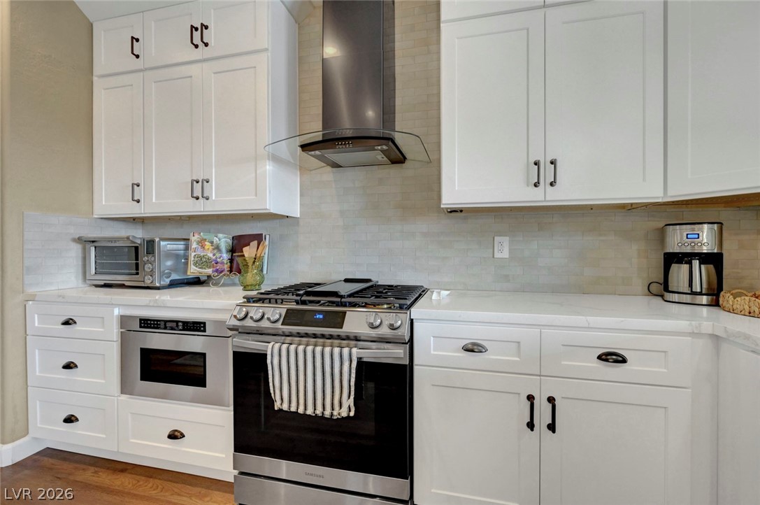 2700 Rue Montpellier Avenue Henderson, NV 89044 - Photo 17 of 39 Kitchen with stainless steel appliances, white cabinets, light stone counters, backsplash, and dark wood-style flooring