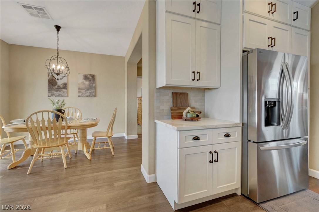 2700 Rue Montpellier Avenue Henderson, NV 89044 - Photo 19 of 39 Kitchen featuring stainless steel fridge with ice dispenser, white cabinetry, light wood-type flooring, suspended lighting, and backsplash