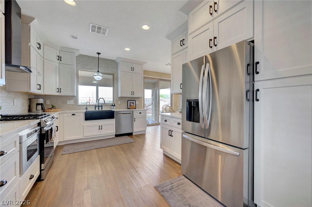 2700 Rue Montpellier Avenue Henderson, NV 89044 - Photo 4 of 39 Kitchen with stainless steel appliances, white cabinetry, light wood-type flooring, and light stone counters