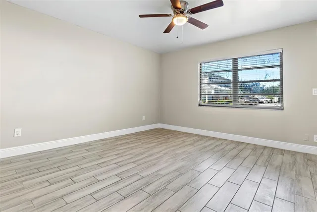 an empty room with wooden floor fan and windows