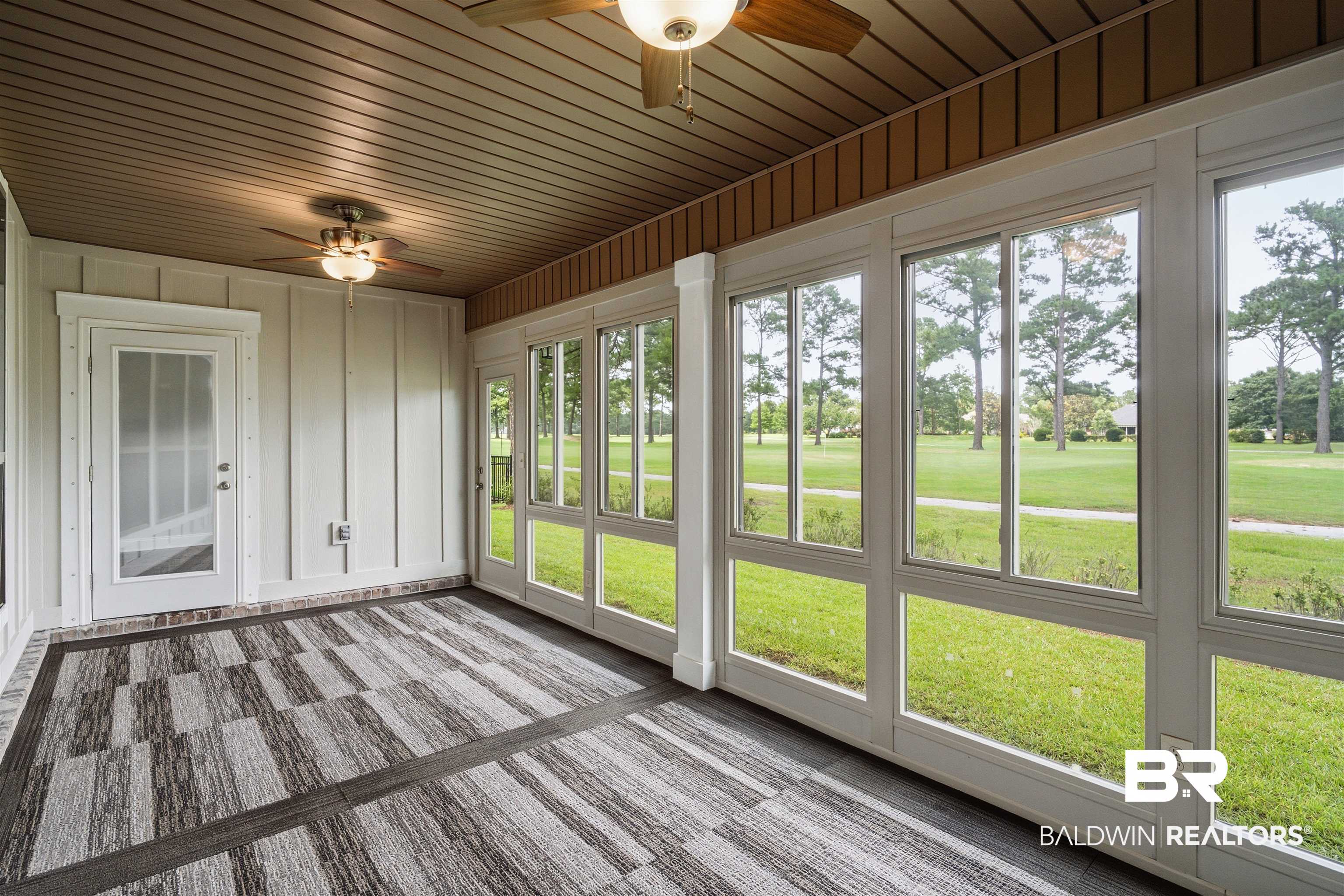 245 Divot Loop Fairhope, AL 36532 - Photo 21 of 26 Screened porch featuring large windows, wood-finish ceiling, two ceiling fans with integrated lighting, a white panel-style door, and geometric pattern flooring