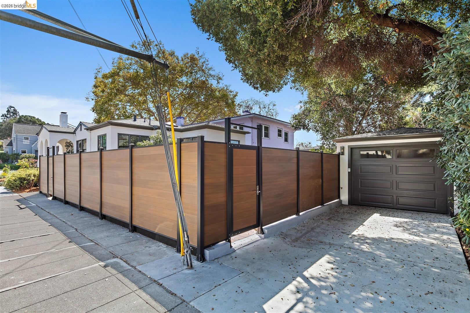 1668 Arch Street Berkeley, CA 94709 - Photo 49 of 78 Wood-finish privacy fence with metal framing, concrete driveway, and attached garage with a dark panel door