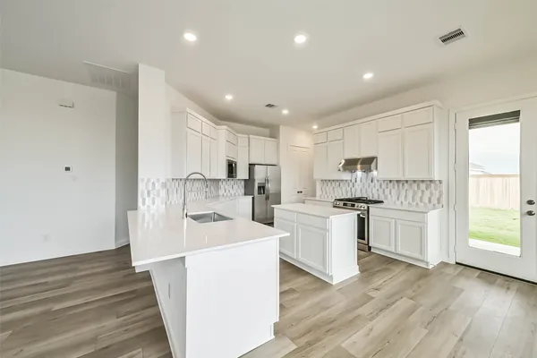 a kitchen with a sink a stove a refrigerator and white cabinets with wooden floor