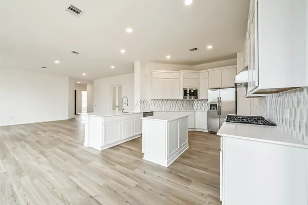 a large kitchen with kitchen island a stove a sink a refrigerator and white cabinets with wooden floor