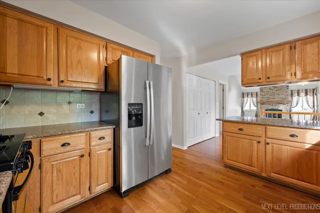 a kitchen with stainless steel appliances granite countertop a refrigerator a sink dishwasher and wooden cabinets with wooden floor