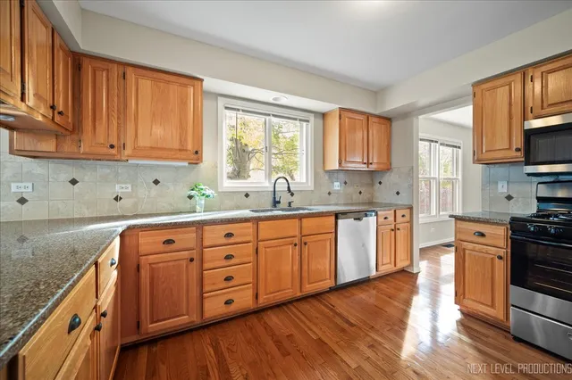 a kitchen with stainless steel appliances granite countertop a stove a sink dishwasher and white cabinets with wooden floor