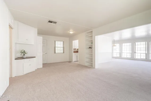 a view of an empty room with a window and kitchen view